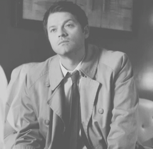 Man In Trench Coat And Tie Sitting On Couch GIF
