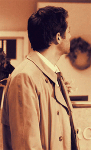 Man In Trench Coat And Tie Standing In Front Of CC Sign GIF
