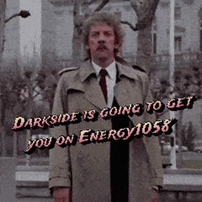 Man in Trench Coat in Front of Darkside Is Going To Get You On Energy 1058 Sign