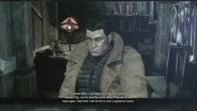 Man In Trench Coat Sitting In Dark Room Talking To Another Man GIF