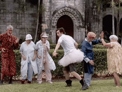 Man In Tutu Dancing With Elderly People In Front Of Building GIF