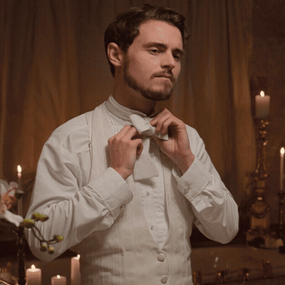 Man In Tuxedo Adjusting Bow Tie With Candles GIF