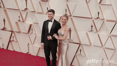 Man In Tuxedo And Woman In Dress On Red Carpet With Oscar Statues GIF