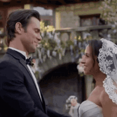 Man In Tuxedo And Woman In Wedding Dress Smiling At Each Other GIF
