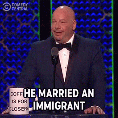 Man In Tuxedo At Podium With He Married An Immigrant Mug GIF