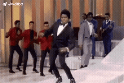 Man In Tuxedo Dancing With Suited Men On Stage GIF
