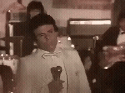 Man In Tuxedo Holding Microphone And Wine GIF
