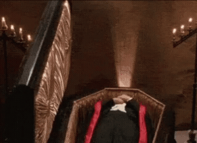 Man In Tuxedo Lying In Coffin With Red Cape GIF