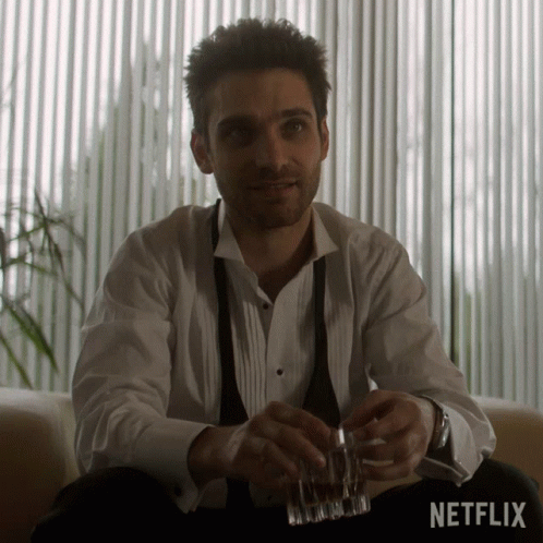 Man In Tuxedo Sitting With Whiskey In Front Of Netflix Sign GIF