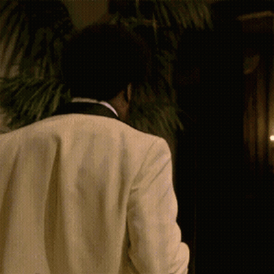 Man In Tuxedo Walking In Dark Room With Palm Tree GIF