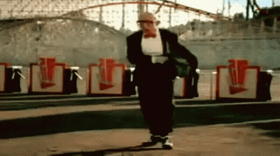 Man In Tuxedo Walking Past Roller Coaster GIF