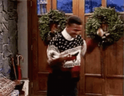 Man In Ugly Christmas Sweater Standing By Door With Wreath GIF