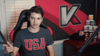 Man In USA Shirt Sitting In Front Of Large K GIF
