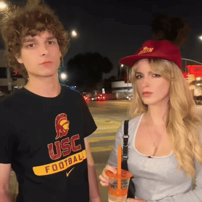 Man In USC Football Shirt Next To Woman In Red Hat GIF