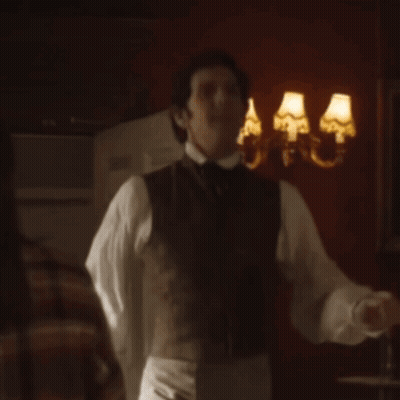 Man In Vest And Tie In Front Of Wall With Three Lamps GIF