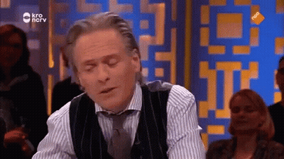 Man In Vest And Tie Sitting In Front Of KRO Screen GIF