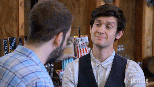 Man In Vest Talks To Another In Front Of Netflix Sign GIF