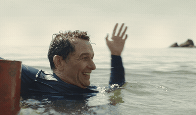 Man In Wetsuit Waving In Ocean GIF