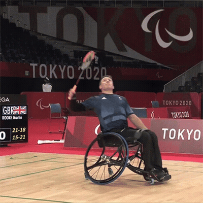 Man In Wheelchair Holding Tennis Racquet In Front Of Tokyo 2020 Sign GIF