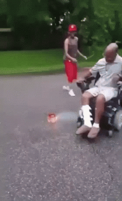 Man In Wheelchair Pushed By Woman In Red Hat GIF