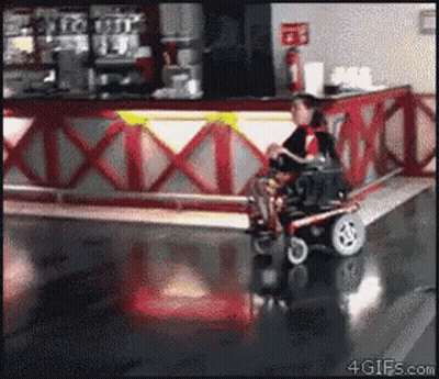 Man In Wheelchair Riding Past Red And White Counter GIF