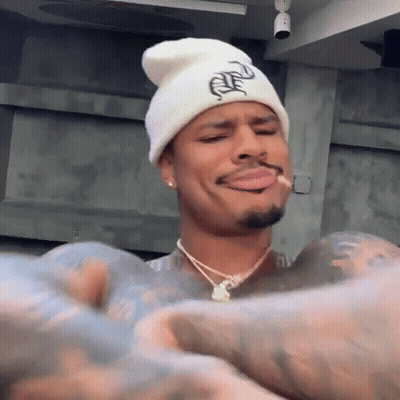 Man In White Beanie And Necklace Smoking Cigarette Making Funny Face GIF