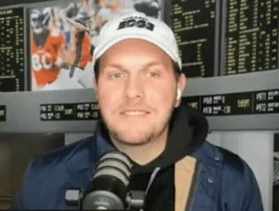 Man In White Hat And Blue Jacket Talking Into Microphone GIF