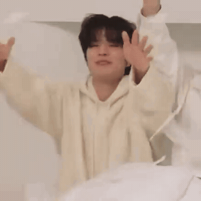 Man In White Hoodie Sitting On Bed With Arms Up GIF