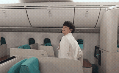 Man In White Jacket Standing In Airplane Looking At Camera GIF