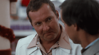 Man In White Jacket Talking To Man In Brown Shirt GIF