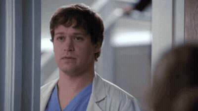 Man In White Lab Coat And Blue Scrubs In Hallway GIF