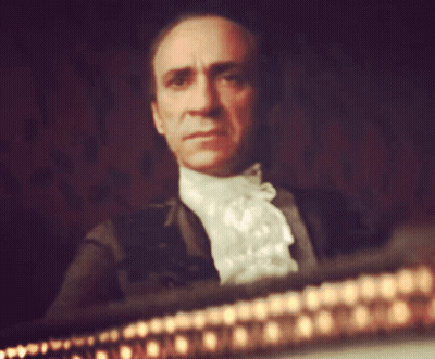 Man In White Lace Collared Shirt Sitting In Dark Room GIF