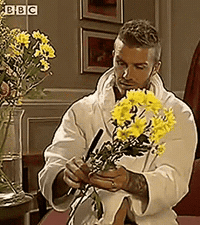 Man In White Robe Holding Yellow Flowers At BBC Sign GIF