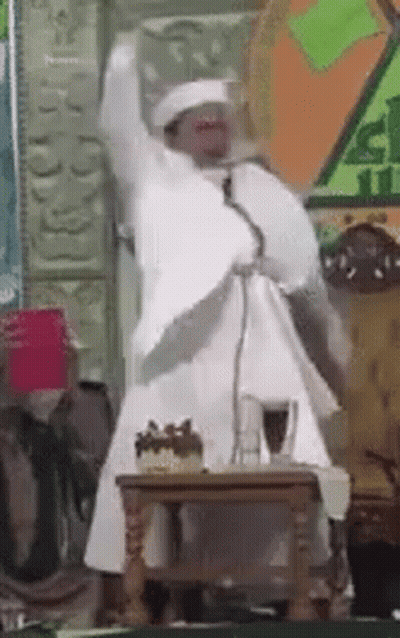 Man In White Robe Speaking At Microphone GIF