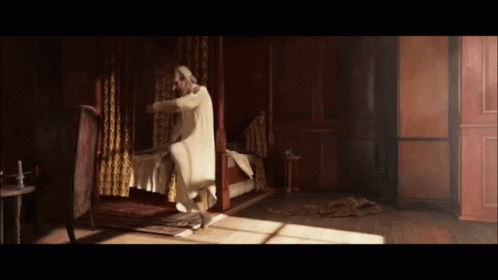 Man In White Robe Standing Next To Bed In Dark Room GIF