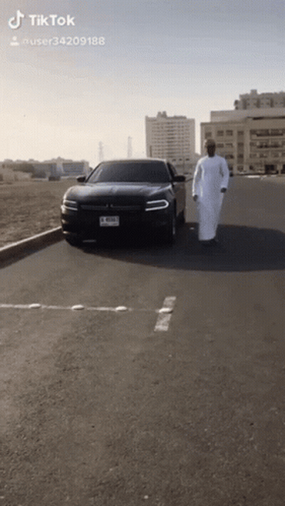 Man In White Robe Walking In Front Of Black Car With License Plate J RSMJ GIF