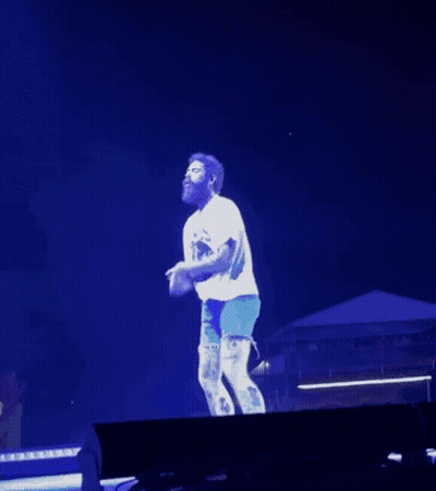 Man In White Shirt And Blue Shorts Dancing On Stage In Front Of Crowd GIF