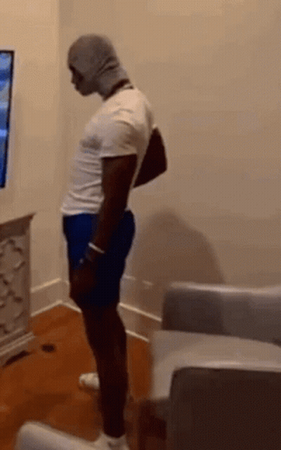 Man In White Shirt And Blue Shorts Standing In Front Of TV GIF