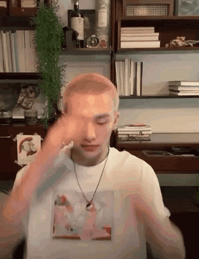 Man in White Shirt and Necklace by Bookshelf