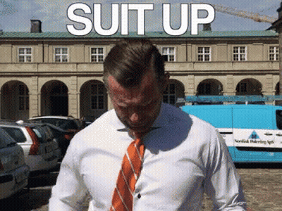 Man In White Shirt And Orange Tie In Front Of Suit Up Building GIF