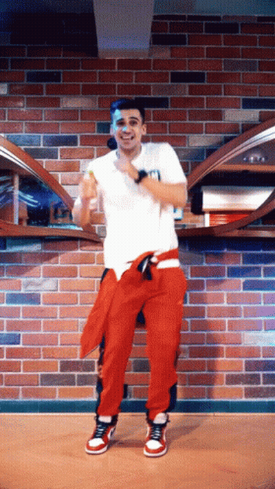 Man In White Shirt And Red Pants Dancing In Front Of Brick Wall GIF