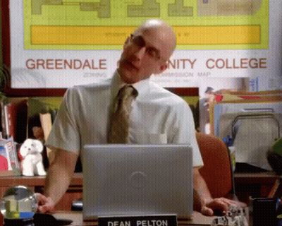 Man in White Shirt and Tie at Greendale Community College Sign