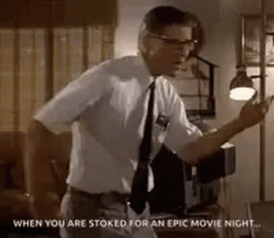 Man In White Shirt And Tie Standing In Living Room With Lamp GIF