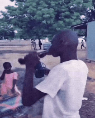 Man In White Shirt Drinking From Bottle Outside GIF