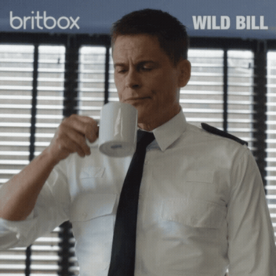 Man In White Shirt Drinking From Mug With Britbox Wild Bill Behind Him GIF