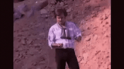 Man In White Shirt Holding Binoculars On Rocky Hill GIF