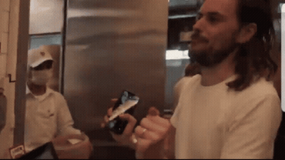 Man In White Shirt Holding Cell Phone In Front Of Masked Man GIF