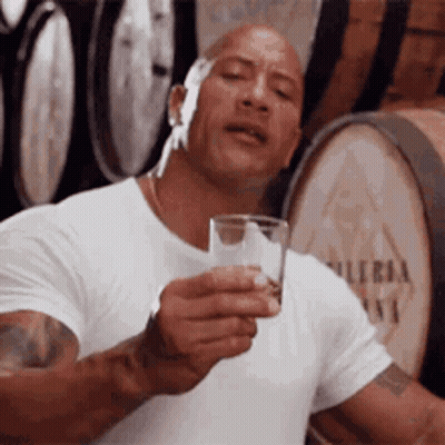 Man In White Shirt Holding Glass Of Water In Front Of Barrels GIF