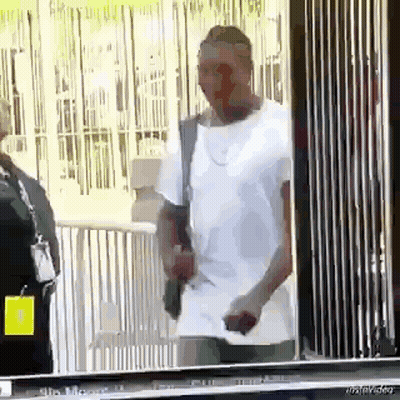 Man In White Shirt Holding Gun In Front Of Fence GIF
