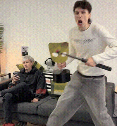 Man In White Shirt Holding Stick In Front Of Couch GIF